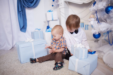 Two boys sitting on the floor with gifts box near Christmas tree