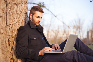 A young man in a park relaxing with laptop computer