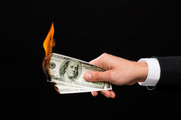 close up of male hand holding burning dollar money