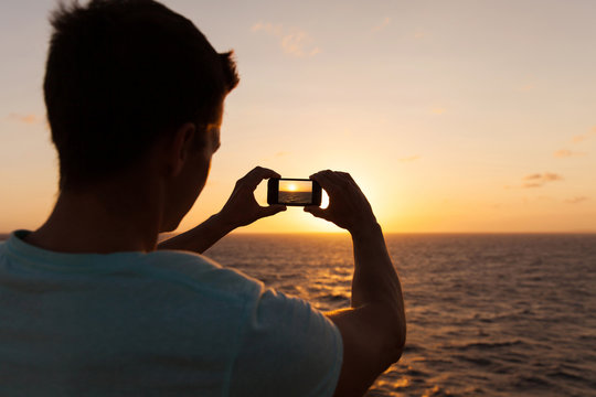 man taking picture of sunset over sea