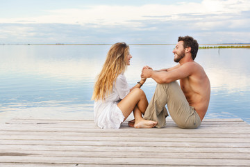 man and woman couple sitting on a jetty under a blue cloudy sky
