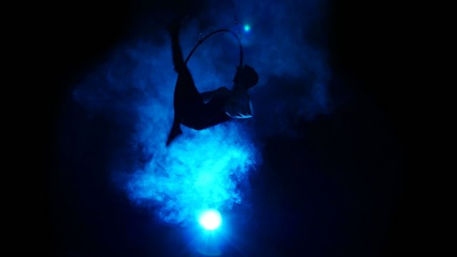 Aerial acrobat man on circus stage. Silhouette on a blue