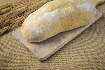 Bread on Bread Board with Wheat on Burlap Background