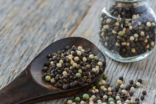 Peppercorn on a Wooden Spoon next to a jar filled with peppercor
