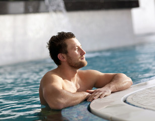 Young man leaning at edge of swimming pool  - 74466972
