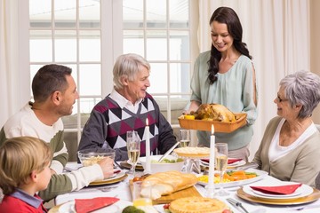 Woman holding turkey roast with family at dining table