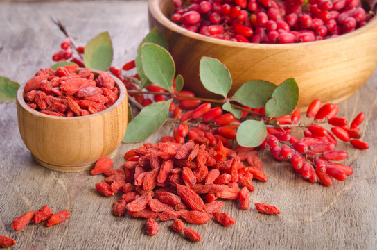 Barberry and dry goji berries in bowls on wooden background