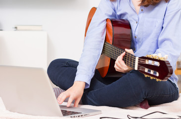 Man playing a guitar and recording her music in computer
