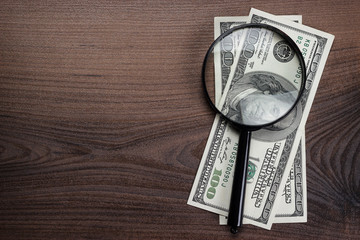 magnifying glass and money on wooden background