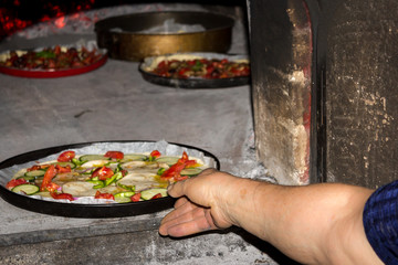 Elderly woman puts pizza into traditional Italian oven