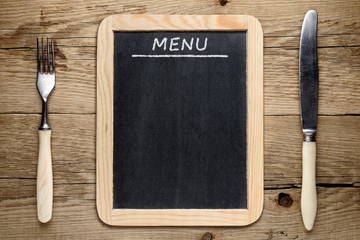 Blackboard menu, fork and knife on old wooden background