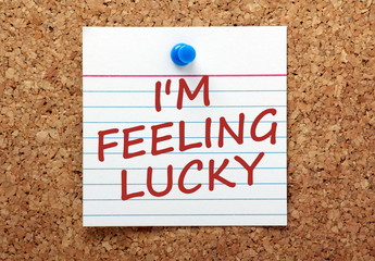 The phrase I'm Feeling Lucky on a card pinned to a cork board