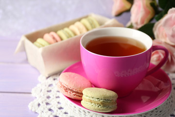 Colorful macaroons with cup of tea on wooden background