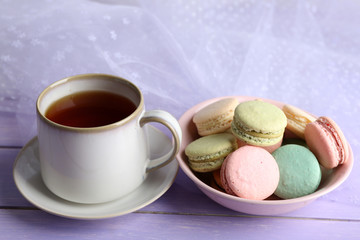 Cup of tea with colorful macaroons on color wooden background