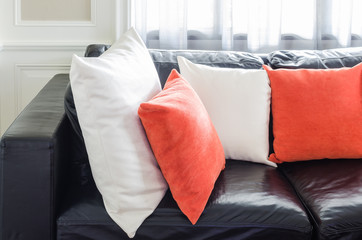 orange and white pillows on modern black sofa in living room