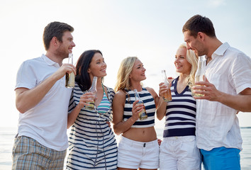 Obraz premium smiling friends with drinks in bottles on beach