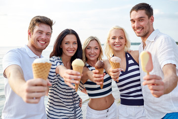 Obraz premium smiling friends eating ice cream on beach