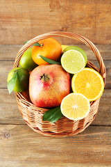 Ripe citrus with green leaves in basket on wooden background