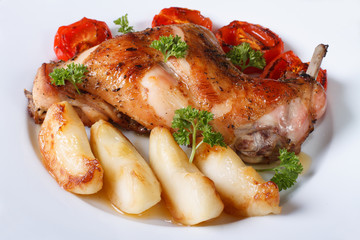 Rabbit leg roasted with apples and tomatoes on a plate close-up