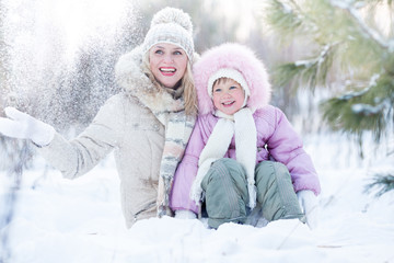 Happy family mother and daughter sitting in snow outdoor