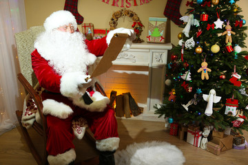 Obraz na płótnie Canvas Santa Claus sitting with list of presents in comfortable chair