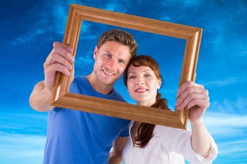 Composite image of couple holding frame ahead of them