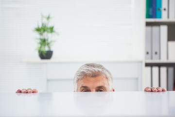 Nervous businessman peeking over desk