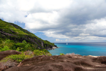 Rocky landscape in the Seychelles with sailboat in the distance