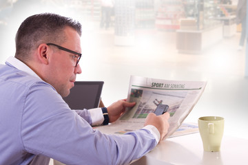 Mann im Hemd liest Zeitung und hält ein Handy