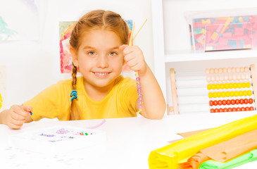 Little beautiful blond girl puts beads on string