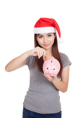 Asian girl with red santa hat put a coin to pink piggy bank