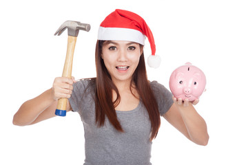 Asian girl with red santa hat hold hammer and  pink piggy bank