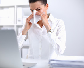 Young businesswoman blowing her nose, sits at the desk
