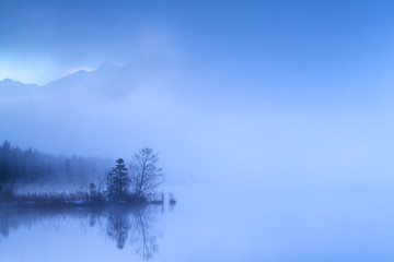 Obraz na płótnie Canvas dense fog in dusk over alpine lake
