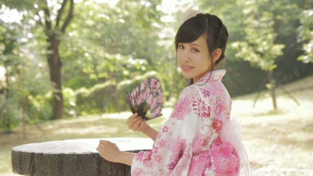 Asian woman in kimono fanning herself in Japanese garden