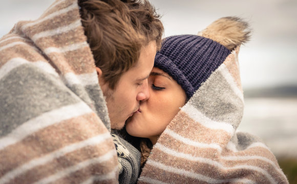 Young couple kissing outdoors under blanket in a cold day