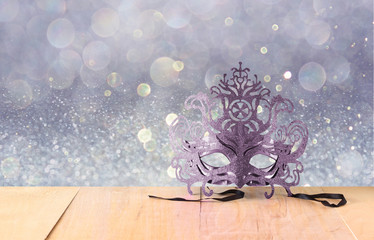 Mysterious Venetian masquerade mask on wooden table and glitter 