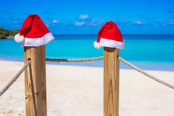 Two red Santa hats on fence at tropical white beach