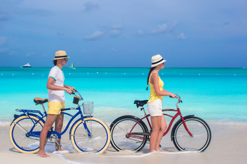 Young happy couple riding bikes on white tropical beach