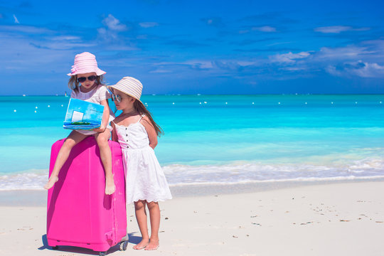 Little girls with big suitcase and map on tropical beach