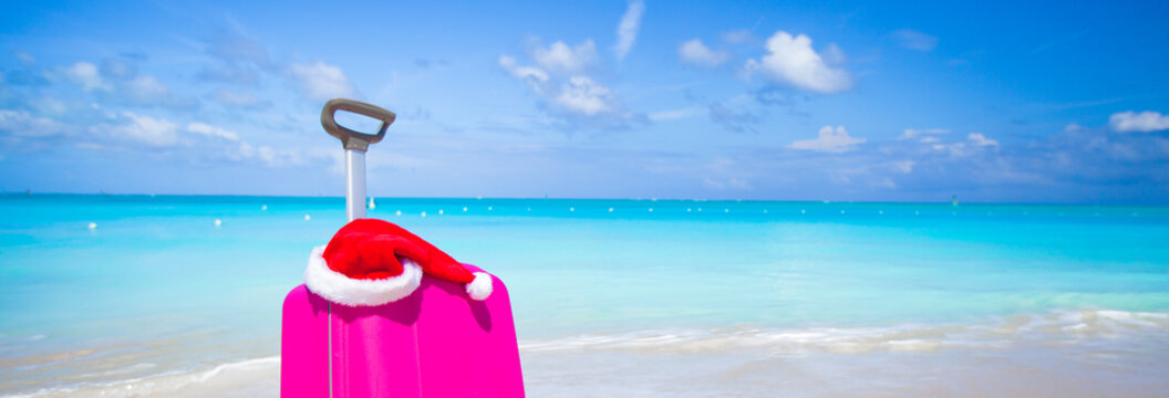 Closeup of pink suitcase and Santa Claus hat on beach