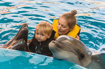 boy and mum float with dolphins in pool