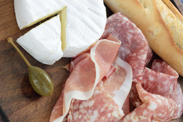 Appetizers board with Camembert, cured ham, salami and capers.