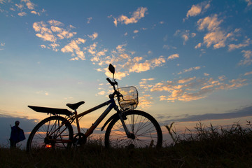Silhouette of mountain bikes with  farmer on grass under sky.