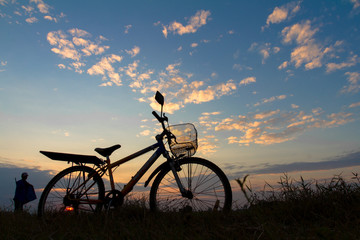 Fototapeta premium Silhouette of mountain bikes with farmer on grass under sky.
