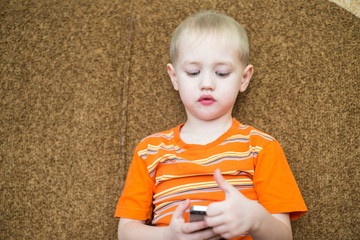 little boy sitting on the couch playing in the smartphone
