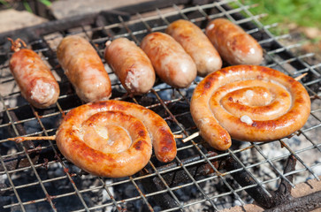 Tasty pork and beef sausages cooking over the hot coals on a bar