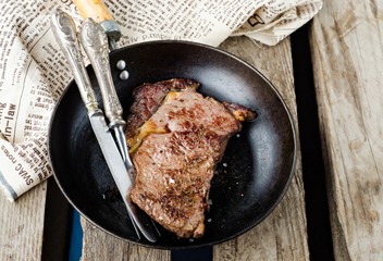 Roasted beef steak antrecot in iron pot on wooden vintage background. Slice of steak