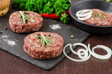 Fresh raw burger cutlets on slate stone black board and wooden background