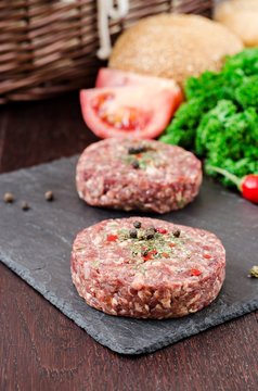 Fresh raw burger cutlets on slate stone black board and wooden background